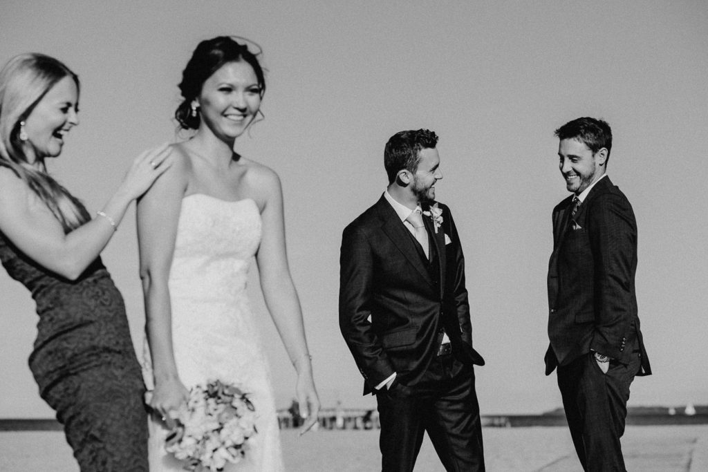 Brautpaar und Trauzeugen lachen am Strand